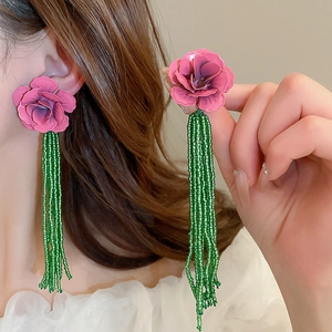 Dettaglio orecchini a fiore con petali magenta e lunghe nappe di perline verdi lucide