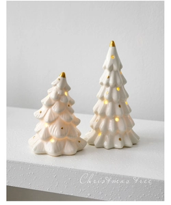Detail of two white ceramic Christmas trees with golden stars and warm LED light effect