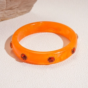 Detailed macro view of orange acrylic resin bangle with red gemstone accents and gold claws