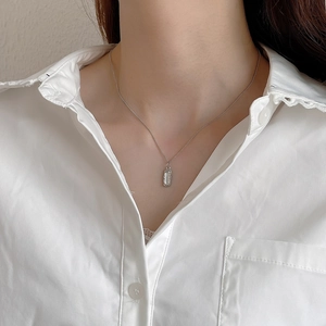 Close-up of irregular textured rectangular pendant necklace on white lace shirt