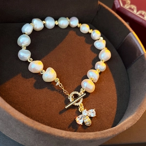 Detailed shot of a baroque pearl bracelet with a gold bee charm and zircon T-bar clasp