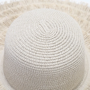 Top-down macro view of spiral woven texture and fringe detail on a beige straw hat