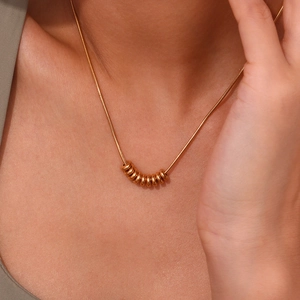 Close-up of golden bean pendant necklace on model with elegant snake chain detail