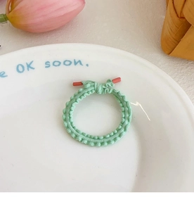 Close-up of mint green elastic hair tie with red cylindrical beads on white ceramic plate
