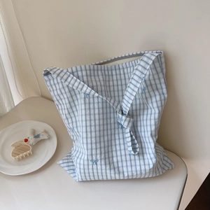 Detailed close-up of blue plaid cotton tote bag with delicate bow embroidery accents
