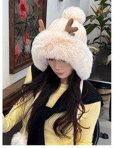 Close-up of beige plush winter hat with festive brown antlers and large faux fur pom-poms