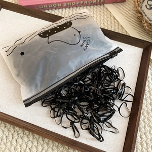 Bulk high-elastic black rubber hair bands in a frosted zipper pouch on a wooden tray