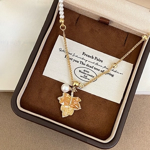 Detail of 18K gold maple leaf pendant with amber crystals and a pearl on a necklace