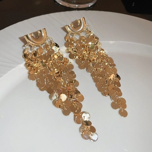 Close-up of gold U-shaped sequin fringe earrings displayed on a white textured plate