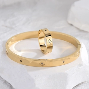 Close-up of gold starburst jewelry set with polished bangle and ring on white stone