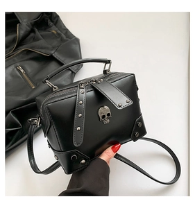Close-up of black leather crossbody bag featuring silver skull emblem and metal rivets