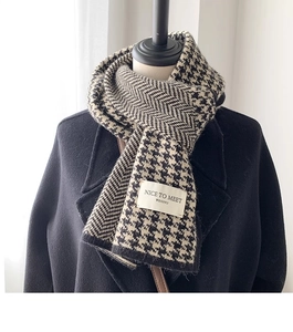 Close-up of houndstooth knit scarf texture with a woven brand tag on black coat