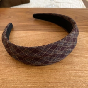Detailed view of the red and brown plaid pattern fabric and black inner lining of the headband