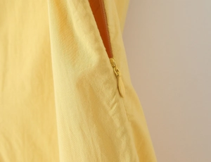 Detailed close-up of a seamless yellow concealed zipper on an asymmetric dress fabric