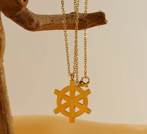 Detailed view of a gold rudder pendant necklace hanging on a natural wooden branch