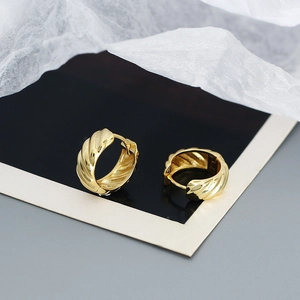 Macro shot of gold twisted croissant huggie earrings on creative paper background