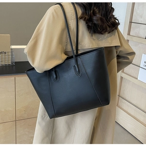 Close-up of a black minimalist leather tote bag styled with a beige trench coat