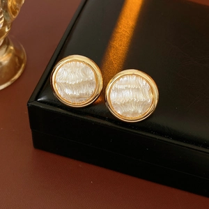 Détail de boucles d'oreilles dorées 16K avec noyau blanc texturé et bordure dorée