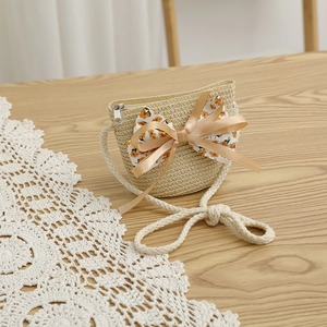 Détail d'un sac bandoulière en paille beige avec nœud floral et sangle en corde de coton
