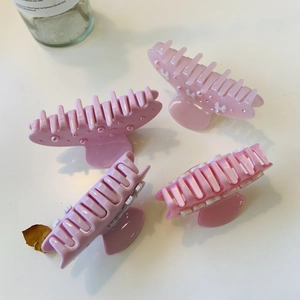 Détail de quatre pinces à cheveux roses en acétate avec perles et nœuds sur fond blanc