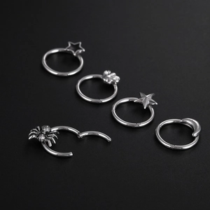 Titanium steel nose rings set with star, moon and spider charms on dark background