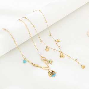 Detail of gold ocean necklaces with sea star, turtle and octopus charms on textured background