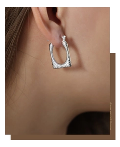 Detail shot of rectangular geometric earrings with vertical textured ridges on a model