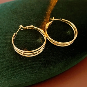 Makroaufnahme goldener mehrlagiger Metall-Creolen auf grünem Samthintergrund