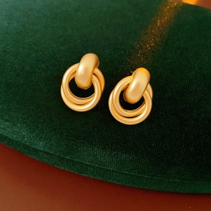 Close-up of golden triple-interlocking metal hoop earrings on green velvet pad