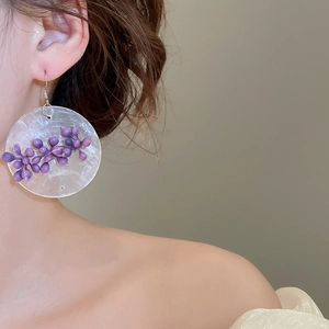Detailed shot of large round drop earrings with purple floral accents on a white base