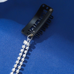 Close-up of a black metal clip with silver rhinestone chain tassel on dark blue background