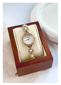 Détail d'une montre dorée avec perles et diamants dans un coffret en bois