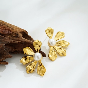 Elegant gold flower earrings with white pearl center on textured wood background