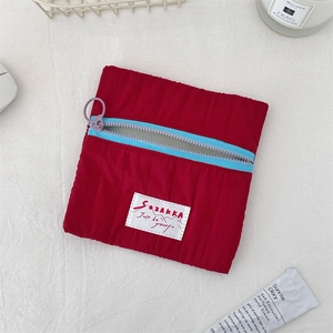 Detail of red quilted nylon cosmetic bag featuring a blue zipper and branded woven label
