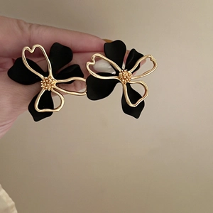 Detail of matte black floral earrings with gold trim held in hand for size context