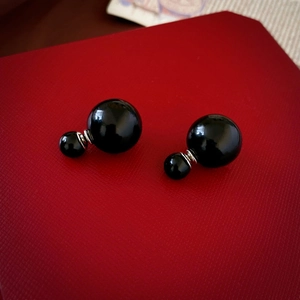 Macro shot of glossy black double-bead earrings on a textured red surface