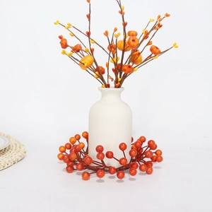 Detail of autumn orange berry wreath and mini pumpkin stems in a white matte ceramic vase