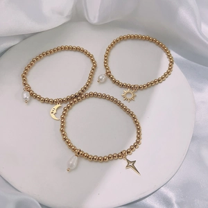 Close-up of three 18k gold beaded bracelets with pearl charms and celestial pendants