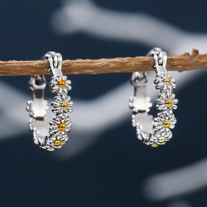 Macro detail of silver daisy hoop earrings featuring yellow centers on a wooden branch