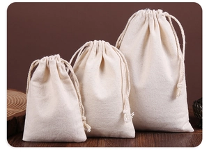 Three assorted sizes of cream canvas drawstring storage bags on a wooden surface