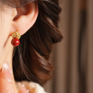 Detailed close-up of a floral gold stud earring with a red bead pendant worn on the ear