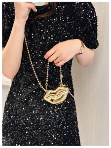 Lip-shaped gold metal mini bag with chain strap carried by model in sequin dress