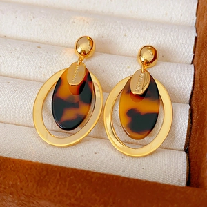 Macro view of handmade gold-plated resin earrings with engraved metal charms in a jewelry box