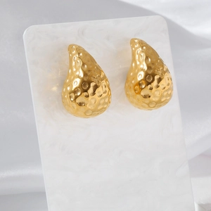 Close-up of golden teardrop earrings with hammered texture on white marble card