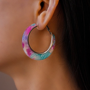 Detailed macro view of large C-shaped resin hoop earring with pink and blue marble pattern