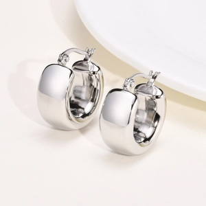 Detailed view of polished silver hollow hoop earrings on a textured beige surface