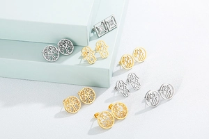 Detail of gold and silver hollow stud earrings with Tree of Life and Hamsa motifs