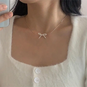 Macro shot of an elegant bow-shaped pearl pendant necklace on a soft white cardigan