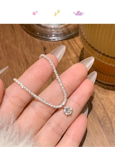 Close-up of a silver tennis bracelet with a round diamond pendant on a wooden background