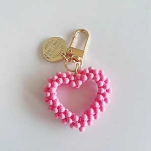 Close-up of pink beaded heart keychain with gold clasp and engraved round metal tag